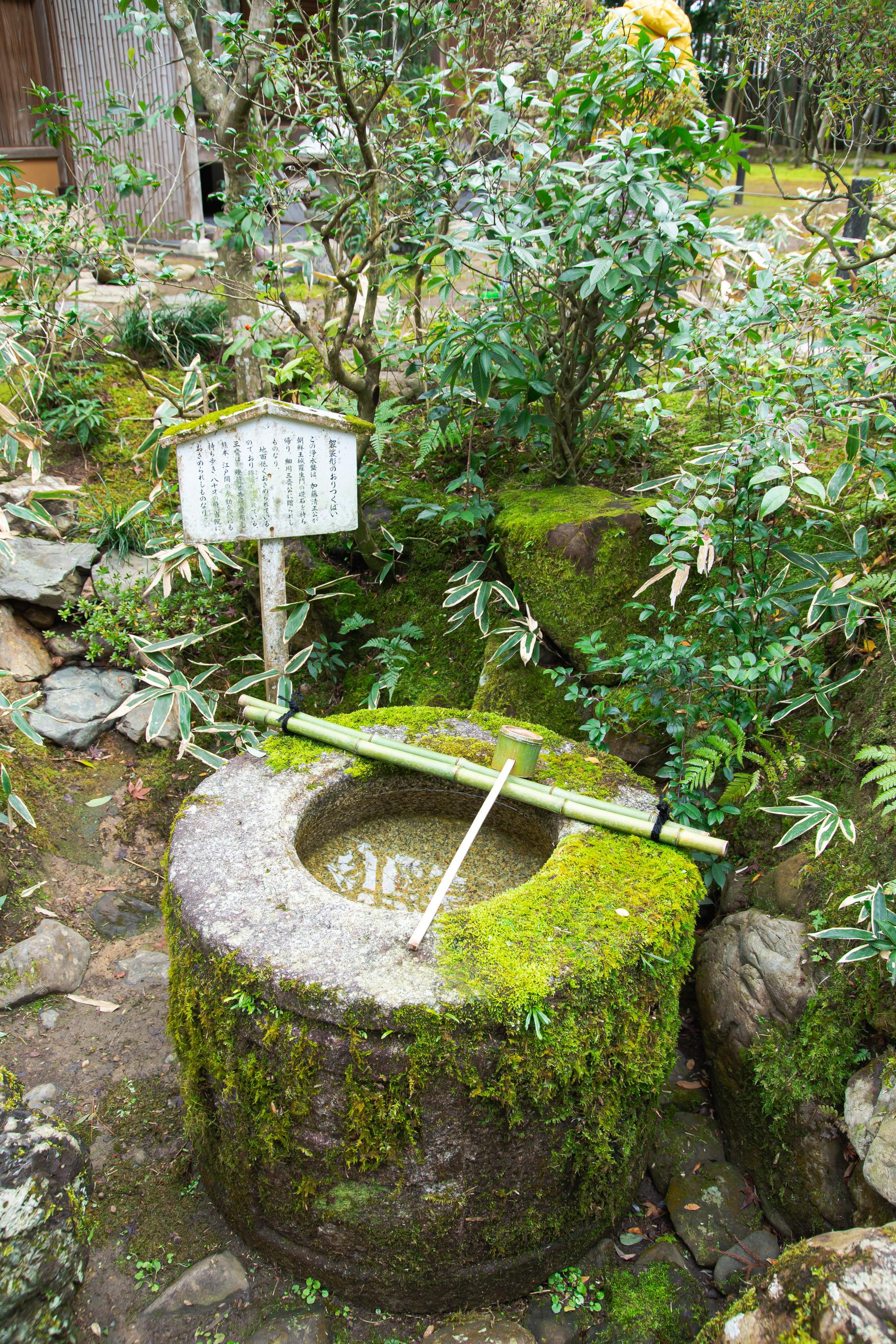 a moss covered stone fountain in front of a Japanese shrine sign in a garden